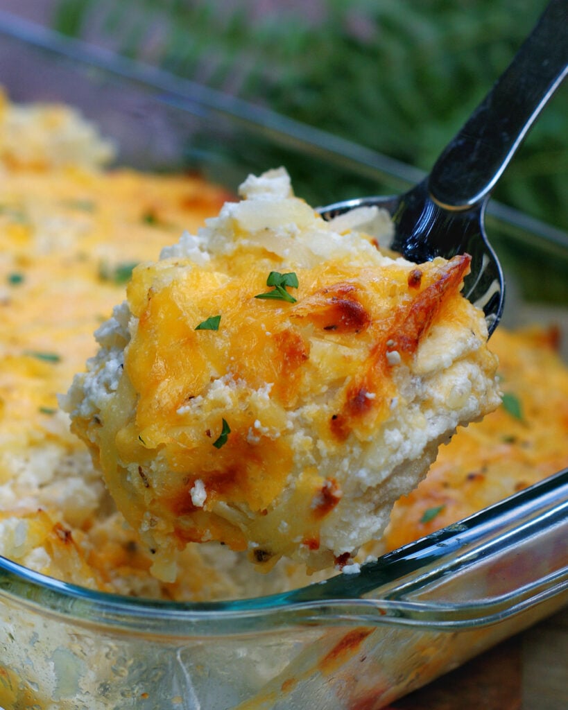 Serving a spoonful of this creamy hash brown casserole topped with melted sharp cheddar cheese.