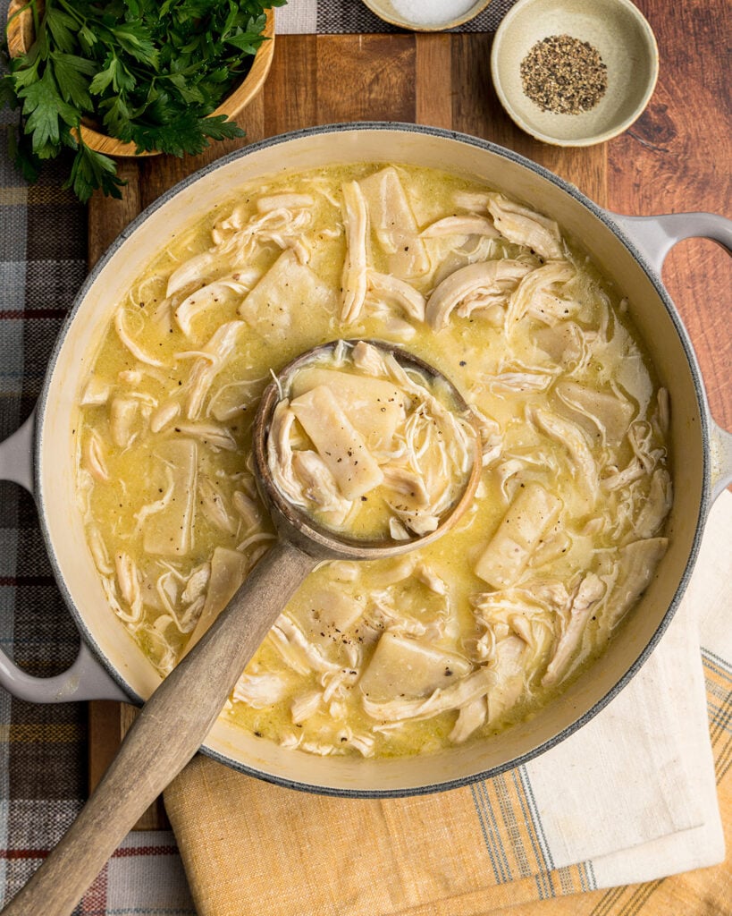 A pot of homemade chicken and dumplings with a wooden ladle for a comfort food dinner idea.