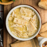 Looking down on a bowl of chicken and dumplings to show the size of the flat dumplings, the shredded chicken and creamy broth.