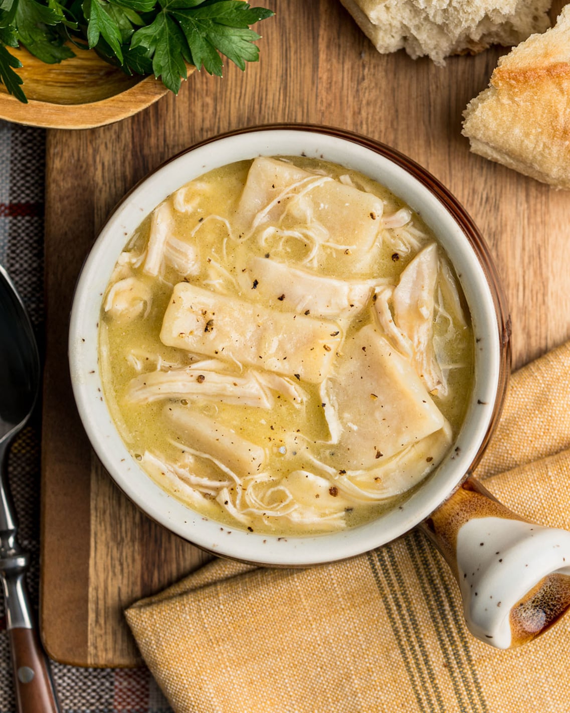 Looking down on a bowl of chicken and dumplings to show the size of the flat dumplings, the shredded chicken and creamy broth.
