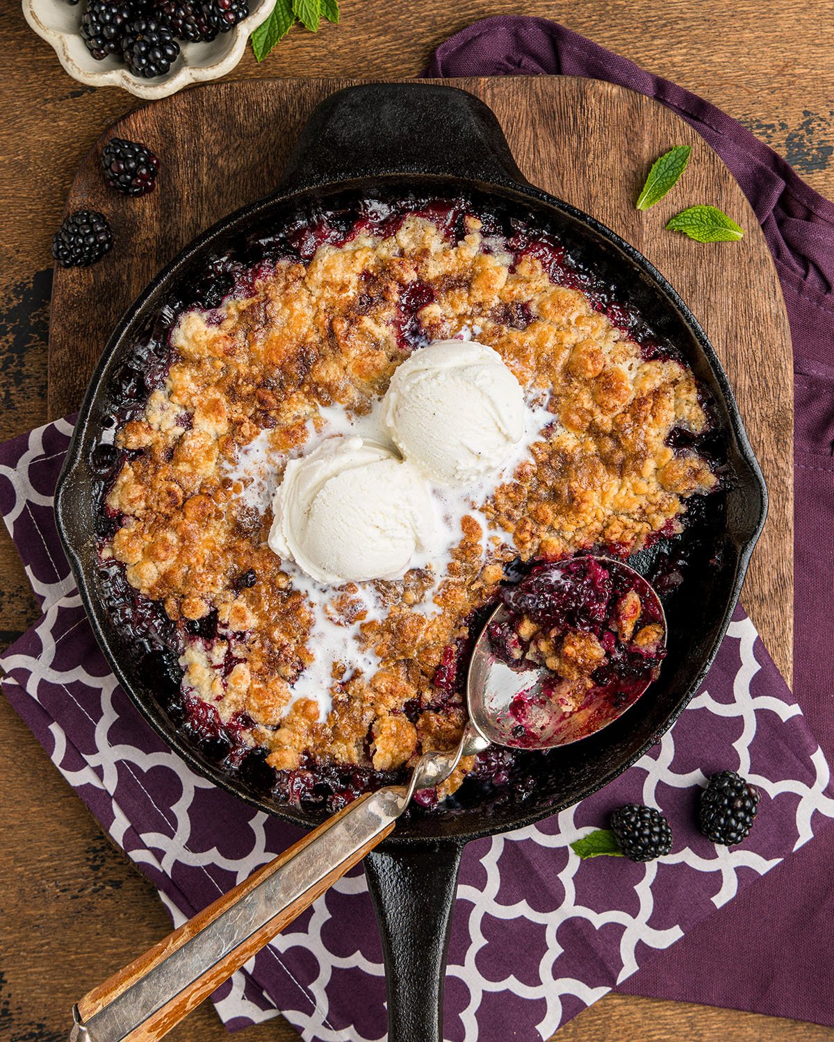 Easy southern blackberry cobbler made in a skillet with two scoops of vanilla ice cream in the center.