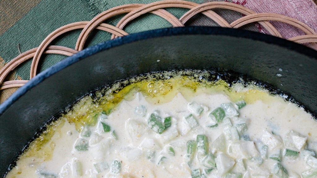 Cornbread batter poured into a hot skillet with the oil bubbling around the edges to show how to make a crispy cornbread bottom.
