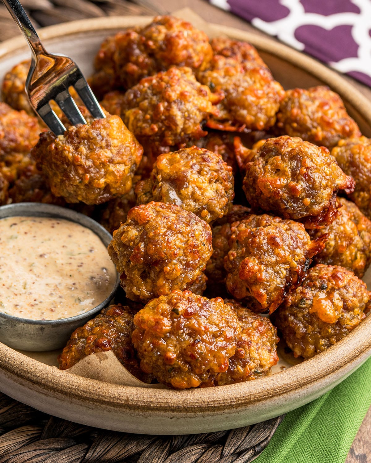 Sausage balls being dipped in creole mustard using a fork.