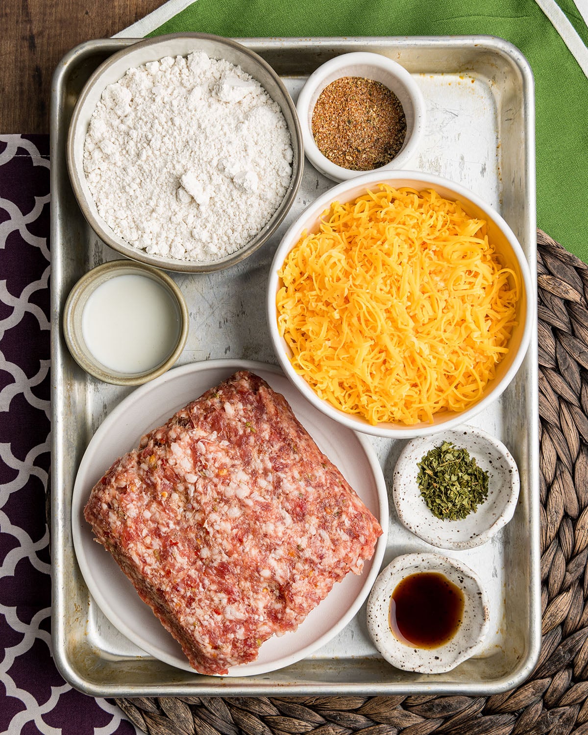 The ingredients needed to make creole sausage balls, including cajun seasoning mix, sharp cheddar cheese and ground sausage meat.