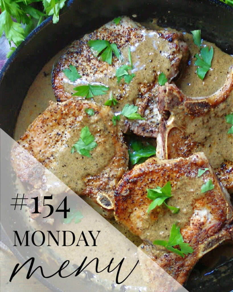 a skillet with smothered pork chops with a text overlay of Monday Menu #154 as this week's meal plan feature recipe.