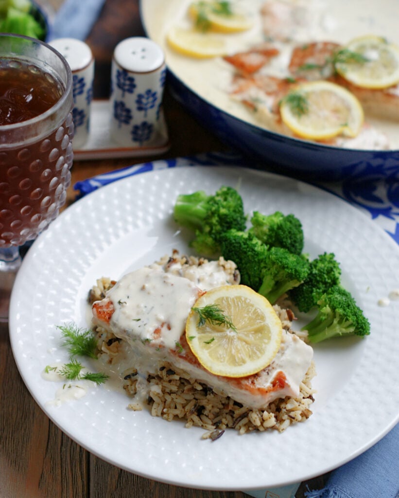 Salmon with creamy lemon dill sauce served over wild rice and with roasted broccoli as a simple dinner idea.