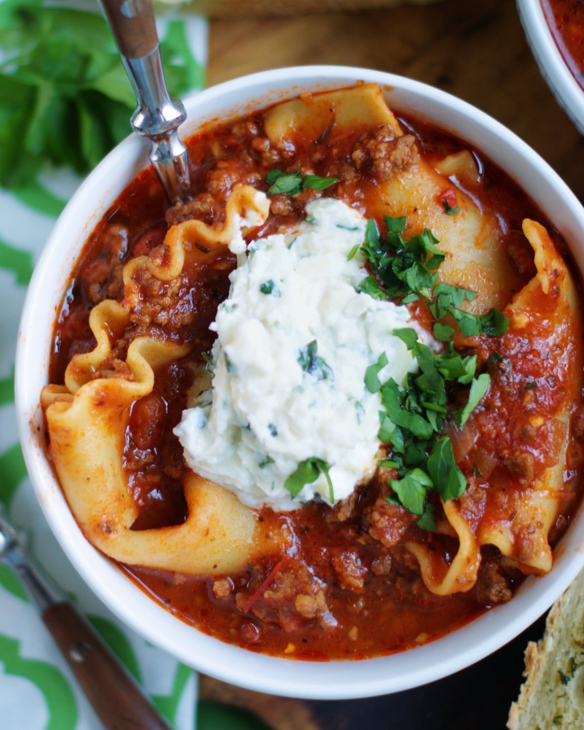 Looking down on a bowl of hearty lasagna soup, full of pasta, meat sauce and a dollop of ricotta cheese topping.
