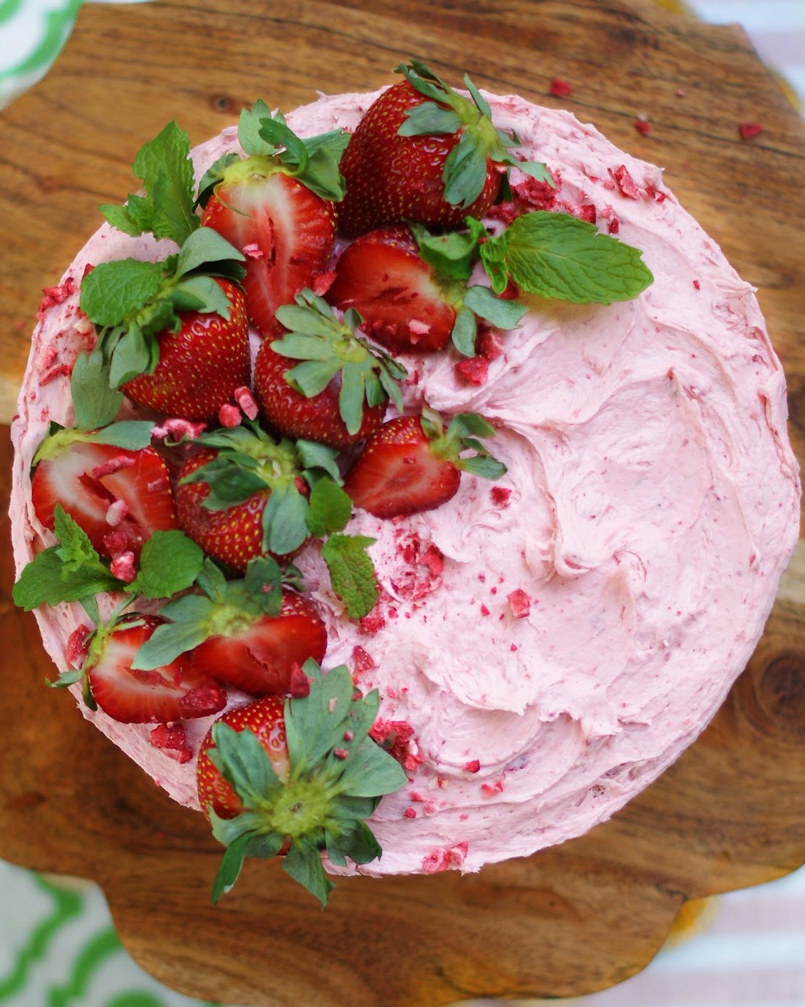The top of an old fashioned homemade strawberry cake, frosted with strawberry buttercream and one half decorated with whole strawberries and halved strawberries as ideas for decoration and presentation.
