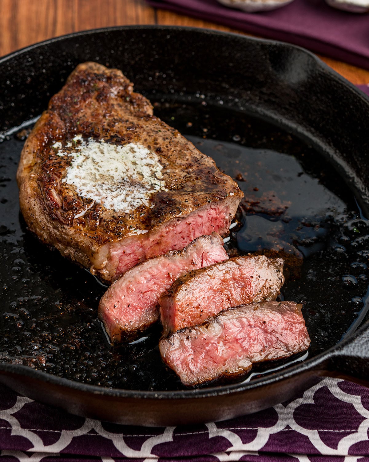 A cast iron skillet seared New York Strip Steak with a pat of butter on top for extra flavor and tenderness.