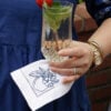 Stacey holding a glass with an apple embroidered cocktail napkin.
