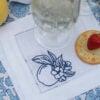 White linen cocktail napkin with hemstitch edge and navy embroidered apple.