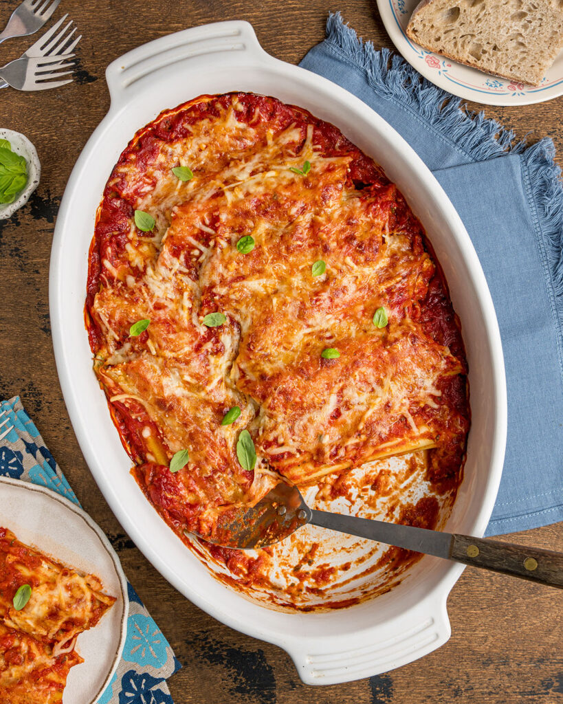 A pan of baked manicotti with melted cheese and marinara sauce.
