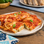A plate of manicotti with one stuffed pasta cut open to show the classic 3 cheese filling.