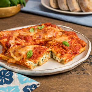 A plate of manicotti with one stuffed pasta cut open to show the classic 3 cheese filling.
