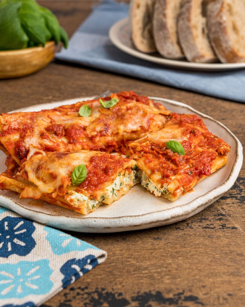 A plate of manicotti with one stuffed pasta cut open to show the classic 3 cheese filling.