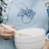 Close up of light blue Southern Discourse apron with navy embroidered apple.