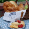 Linen teal towel with embroidered apple lining a bread basket with cheese and fruit.