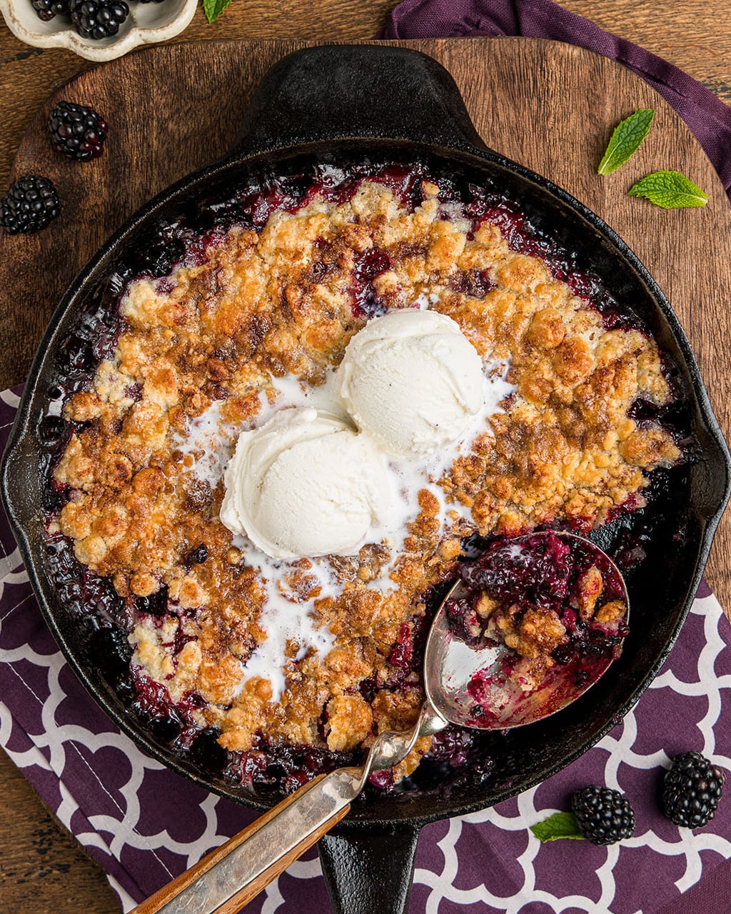 Easy southern blackberry cobbler made in a skillet with two scoops of vanilla ice cream in the center.