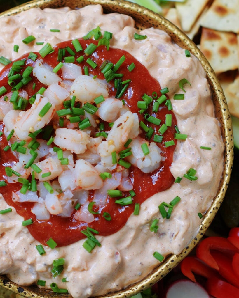 A close look over the top of a bowl of cream cheese and shrimp dip with a cocktail sauce topping, chopped shrimp and chives to show texture and color.