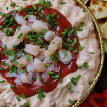 A close look over the top of a bowl of cream cheese and shrimp dip with a cocktail sauce topping, chopped shrimp and chives to show texture and color.