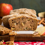 A cinnamon apple bread loaf sliced to show how it is loaded with apples, walnuts, and has sweet crispy crust.