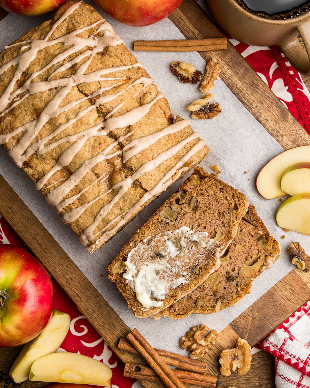 Looking down on freshly baked apple bread to show the drizzle of cinnamon sugar glaze and a slice with melted butter as a serving idea.