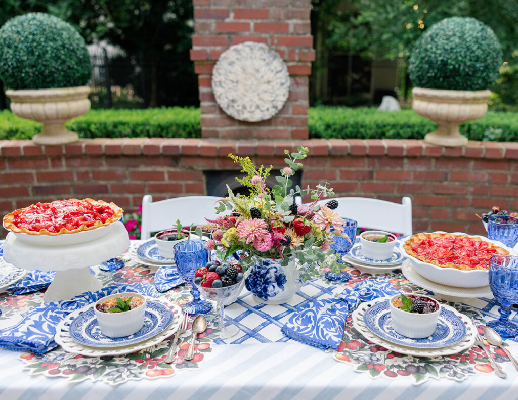 A table set with blue and white with a flower centerpiece filled with berries and berry desserts in the center of the table as inspiration for inviting friends over for dessert.