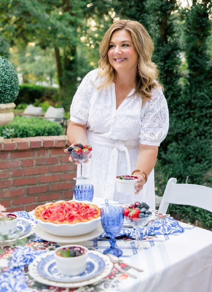The hostess in a white dress setting the table and placing individual cobblers and coupes of fruit at each place setting.