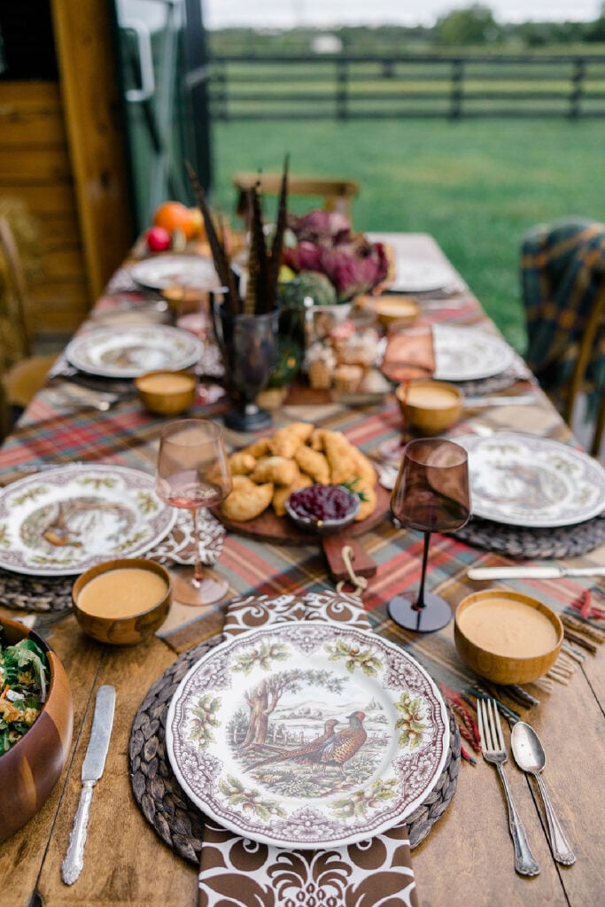 An outdoor Friendsgiving table dressed in browns and plaids with Woodland Spode pheasant plates.