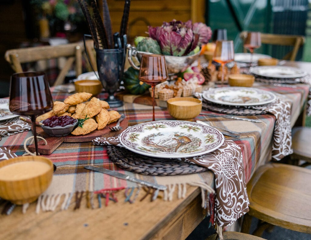 A view of the table setting from the side where the dark rattan placemats, brown print napkins, Woodland dishes, plaid table covering and light brown stemware can be seen.