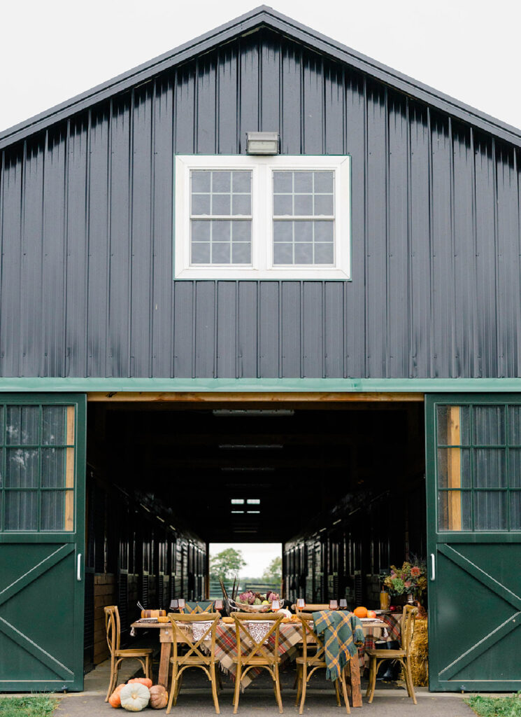 A farm table set up in the entry way of a barn prepared for a Thanksgiving dinner.